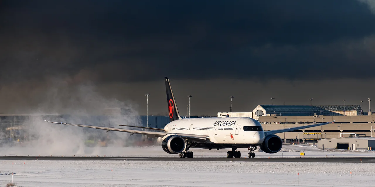 An Air Canada aircraft on a snowy apron with drifting snow behind it.