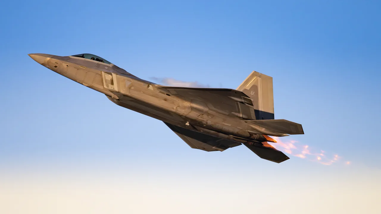 An F-22 fighter jet in flight under soft evening light.