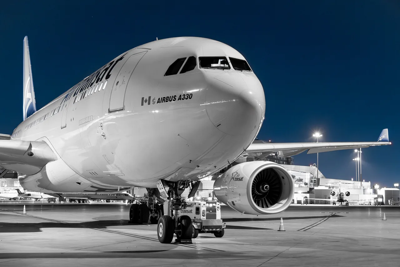 An Air Transat aircraft parked on an illuminated airport apron at night.