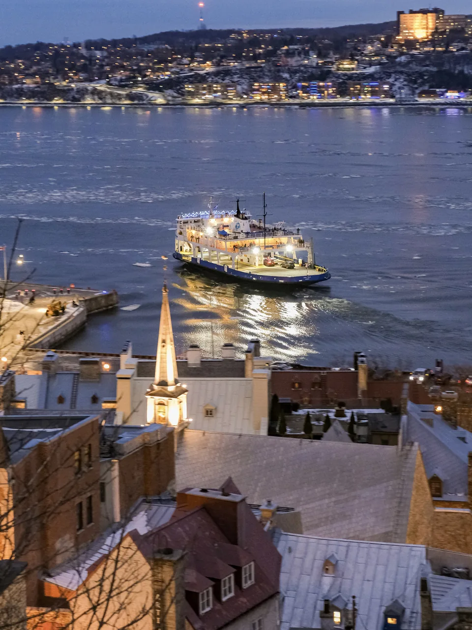 A ferry and riverside buildings after sunset.