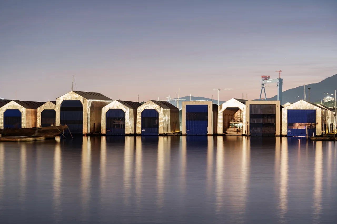 A row of waterfront boathouses reflected in still water.