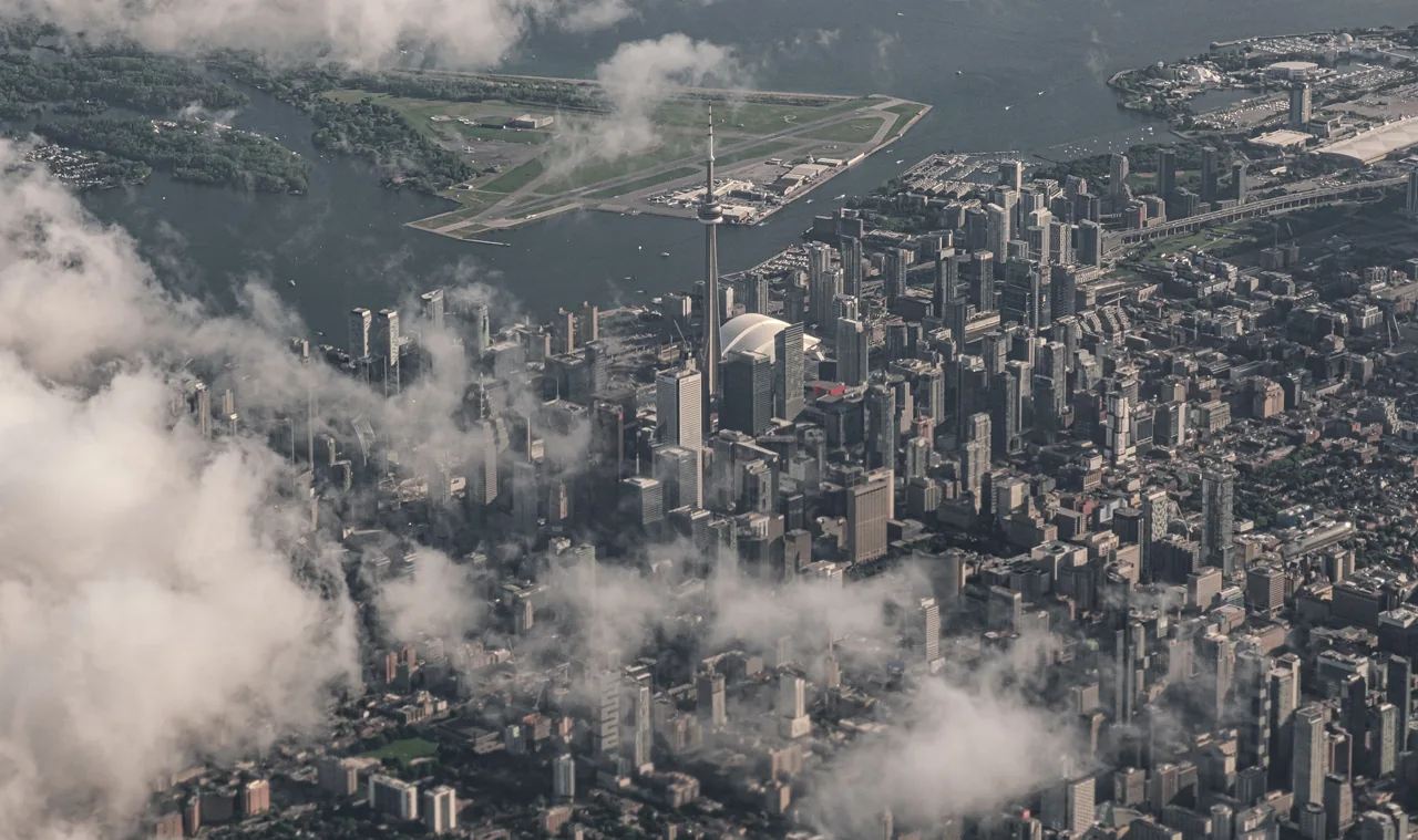 An aerial view of Toronto skyscrapers and the CN Tower through clouds.